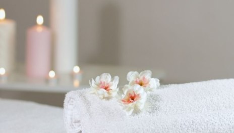 im Vordergrund wei&szlig;e Handt&uuml;cher mit Bl&uuml;mchen, im Hintergrund brennende Kerzen | &copy; Canva/TI Hunsr&uuml;ck-Mittelrhein